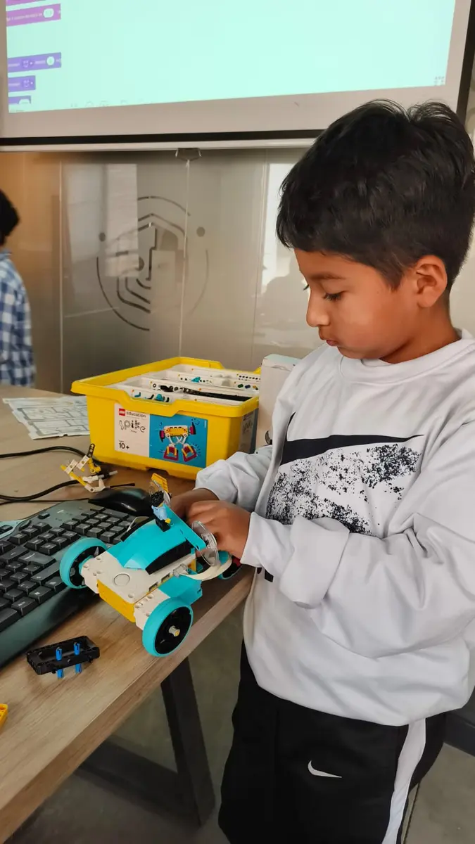 Niño ajustando un robot LEGO Spike Prime frente a la pantalla con bloques de código